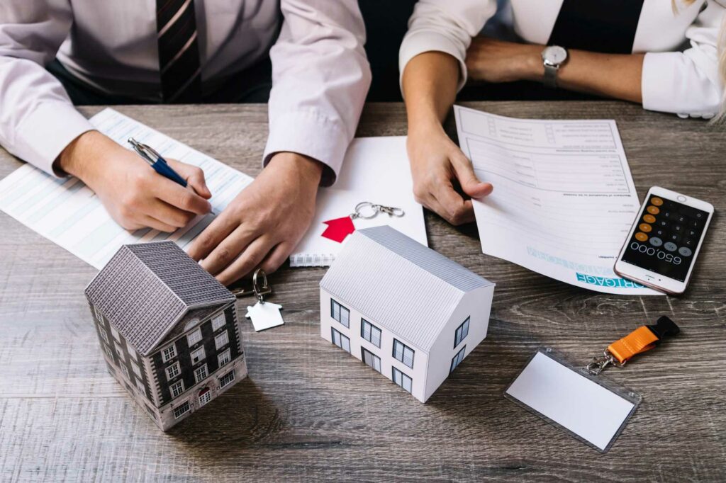 Property solicitor signing a property transaction document with miniature house figures and keys on desk